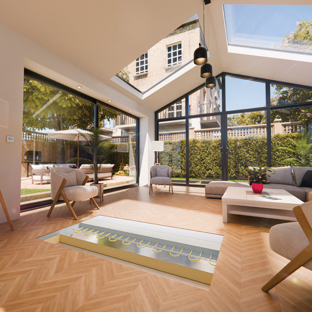A modern open-plan living room with large black-framed glass walls and skylights, showing a garden patio outside. The room features light wood herringbone flooring, a gray sectional sofa, beige armchairs and a white coffee table. There is a cutout in the floor showing the Thermosphere underfloor heating screed cable inbedded in screed on top of xps insulation board.