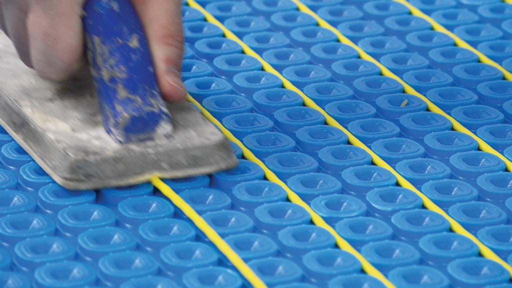 A close-up of a hand using a grout float to place Thermosphere Ultimate heating cable into place on the ultimate matting.