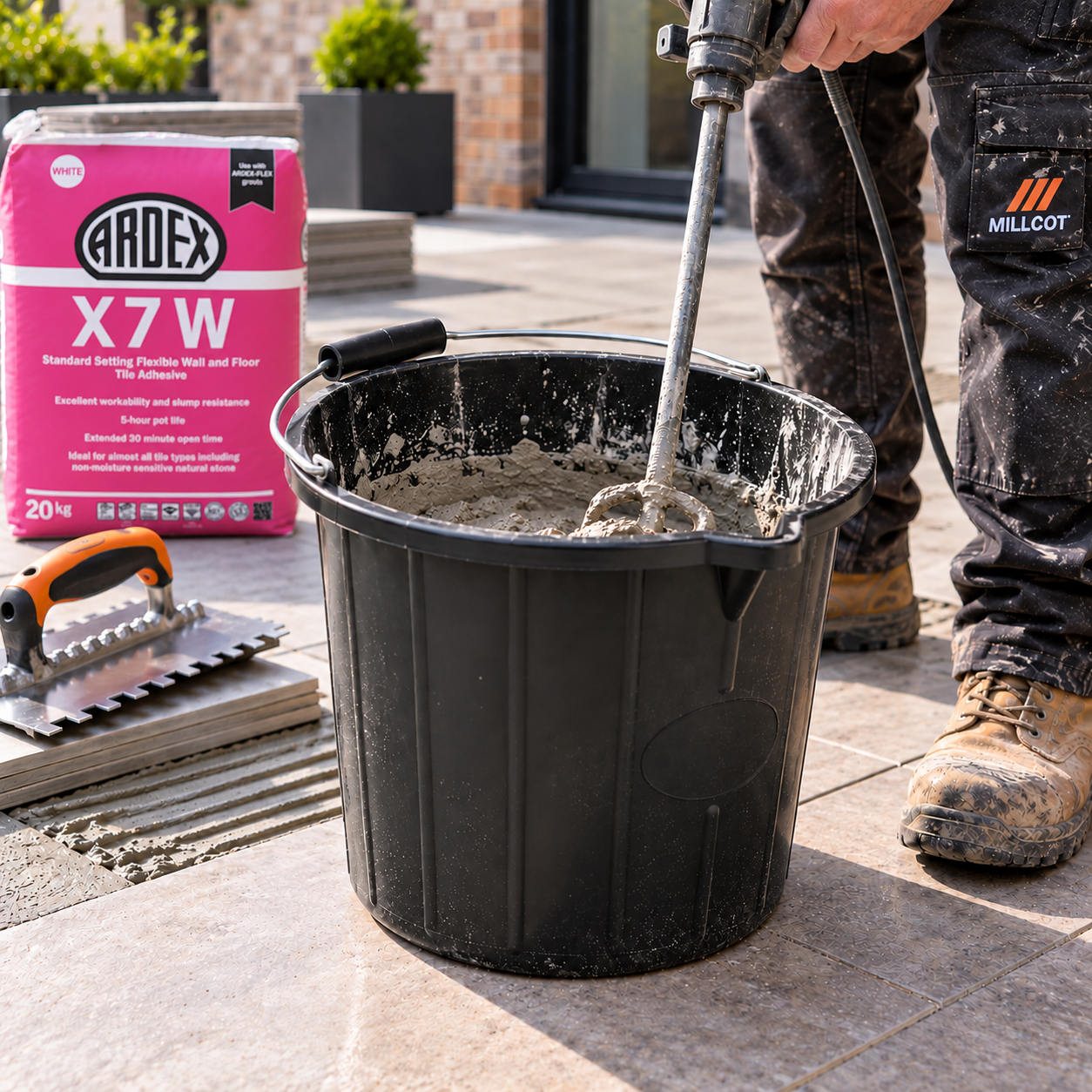 Tiler using a 3 gallon black builders bucket for mixing materials during a tiling job