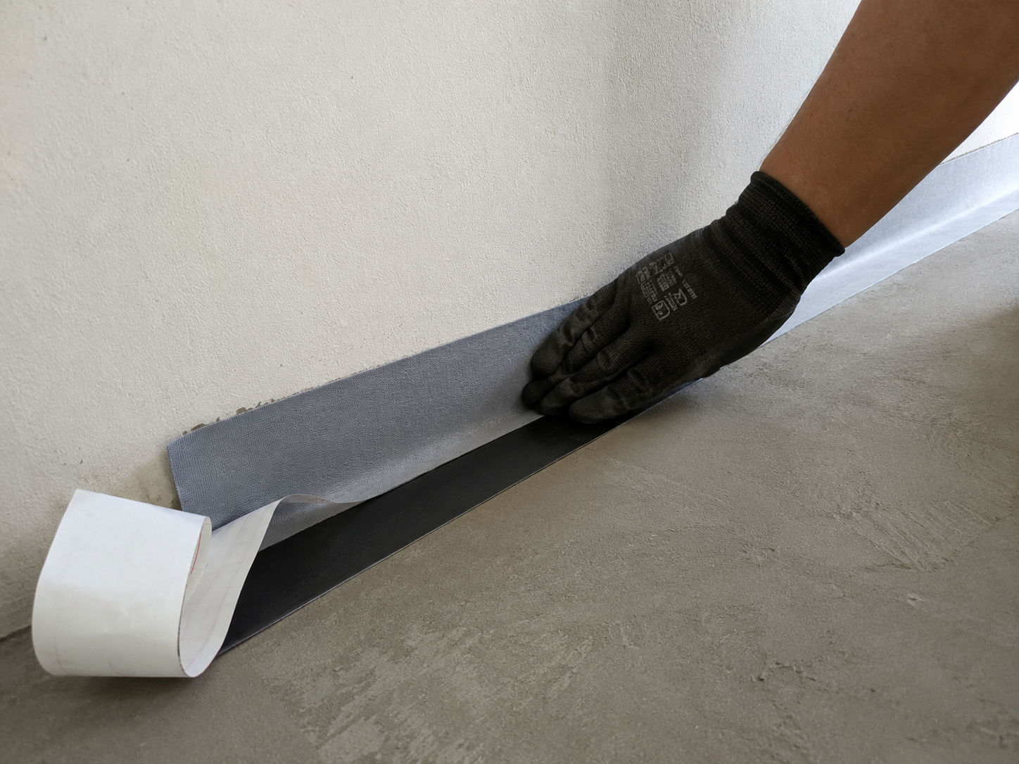 ButylX Pro waterproof skirting tape being applied along floor-wall junction for waterproofing before tiling