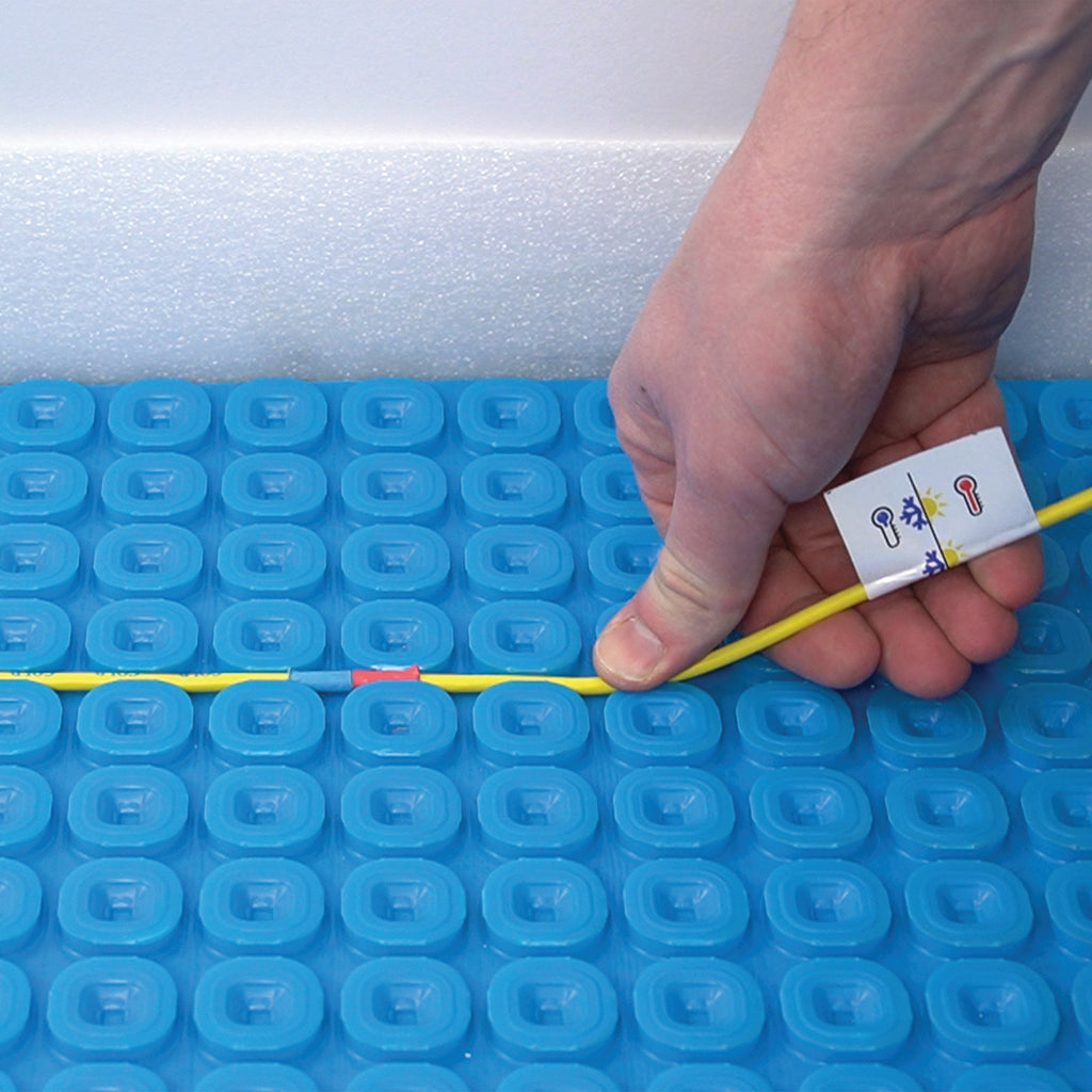 A close-up of a person's hand fixing the yellow Thermosphere ultimate heating cable into place on the ultimate matting